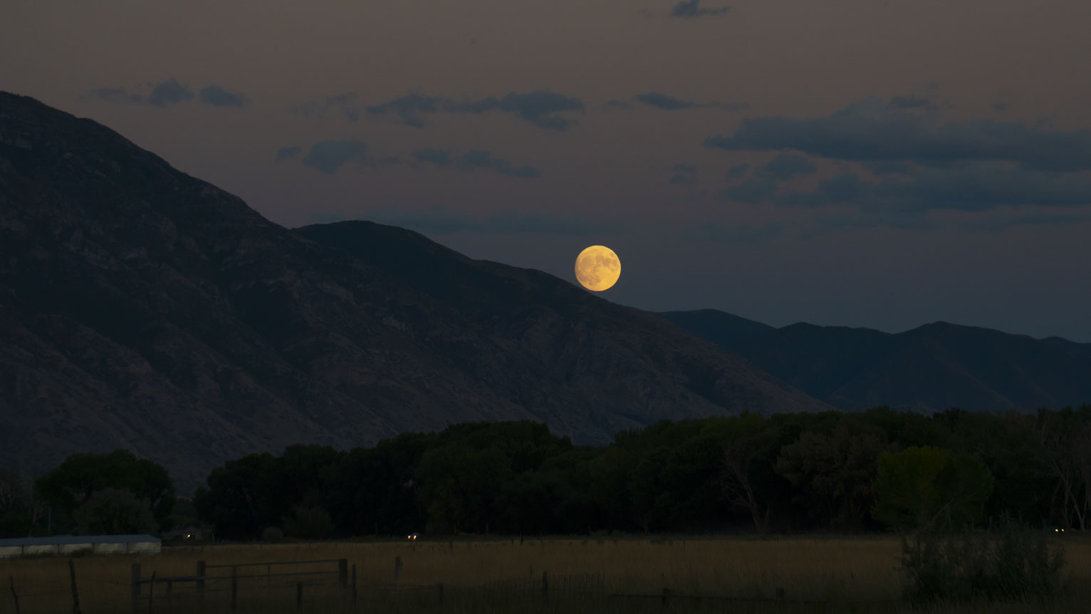 The full moon rises just above the mountain in the dusky sky